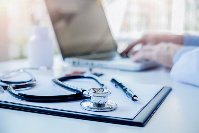 closeup of stethoscope and clipboard as doctor types on a computer